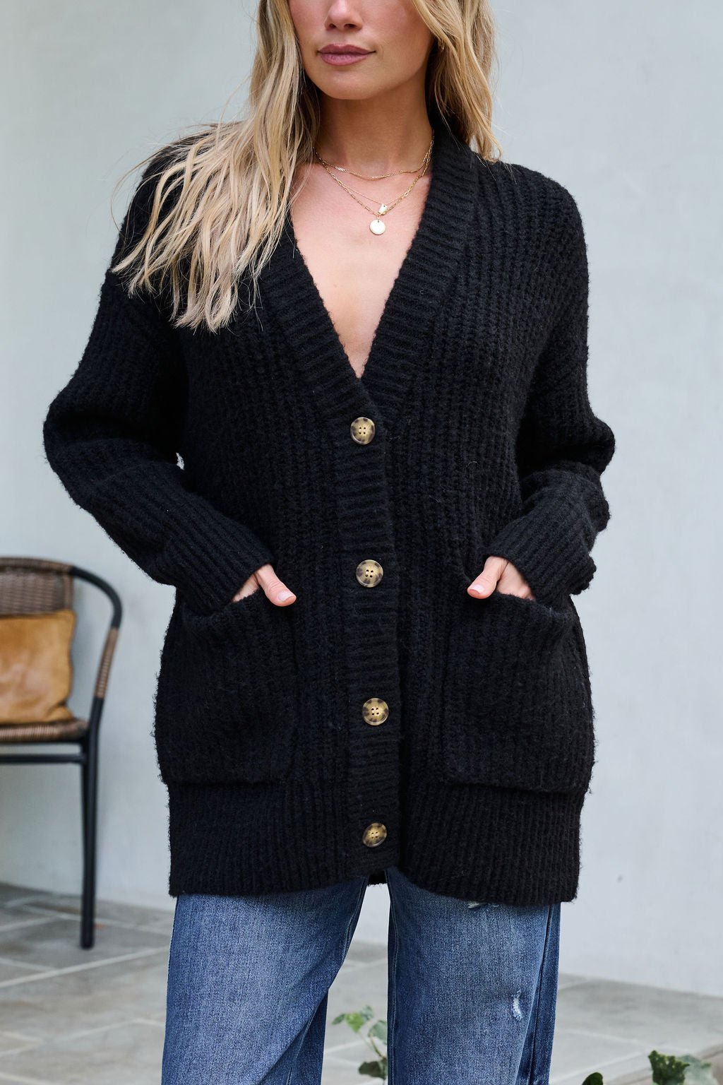 Woman wearing the Basic Black Knit Button Down Cardigan with blue jeans, standing in front of a chair outdoors.