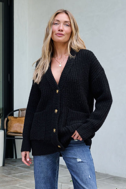 Woman with long blonde hair wears the Basic Black Knit Button Down Cardigan and blue jeans outdoors—your winter wardrobe essential.