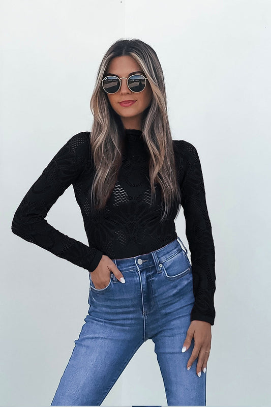 Woman wearing a Black Mock Neck Fishnet Top, high-waisted jeans, and sunglasses against a plain white background.