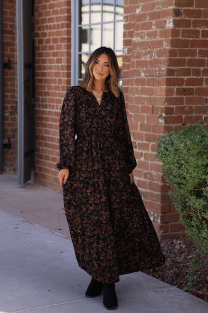 A woman stands outside by a brick wall in the Black Multi Floral Print Tiered Midi Dress.