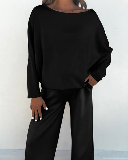 Person wearing the Black Off The Shoulder Scuba Top with matching black pants, standing against a plain light background.