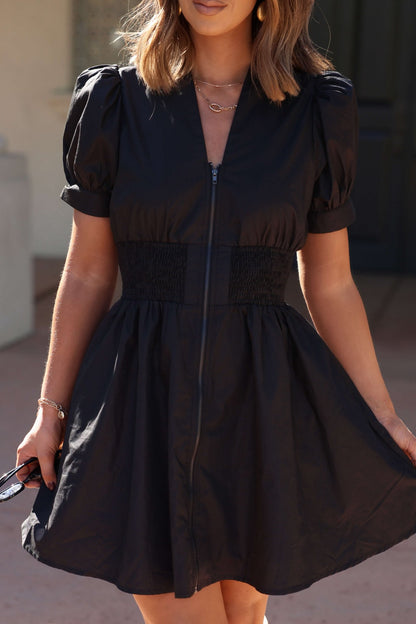 Woman wearing the Black Puff Sleeve Smocked Mini Dress - FINAL SALE, holding sunglasses in one hand.
