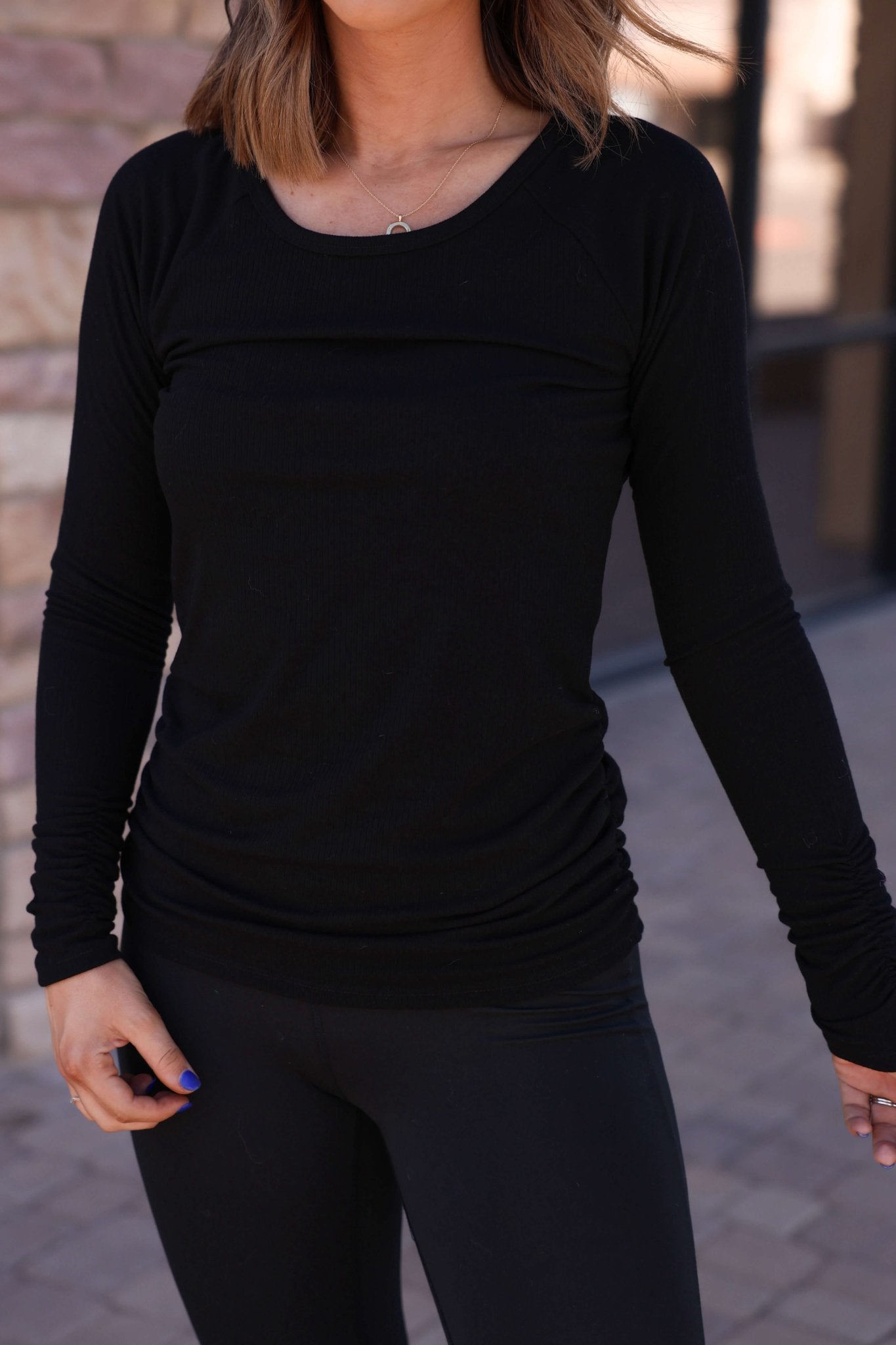 Woman in a Black Ruched Sleeve Ribbed Top - DOORBUSTER and black leggings, highlighting modern women's fashion on a walkway.