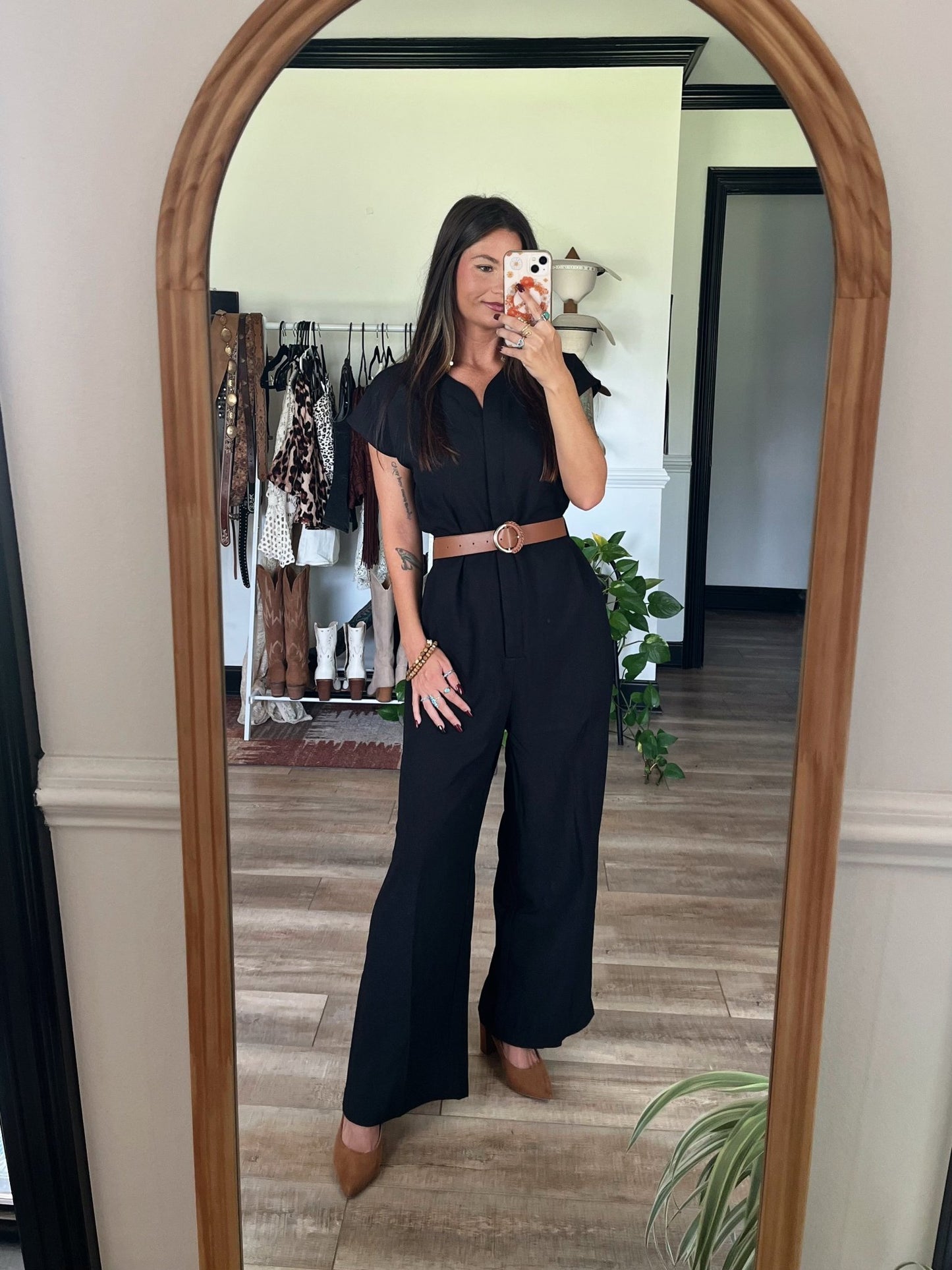 Woman snaps a mirror selfie in the Black Short Sleeve Belted Jumpsuit - DOORBUSTER, styled with brown shoes and chic clothes behind her.