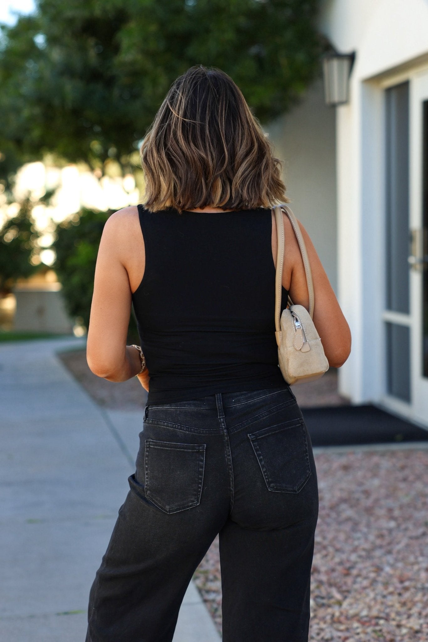 Woman with shoulder-length hair walks outdoors in jeans, carrying a beige purse and wearing the Black Square Neck Double Lined Tank Top.