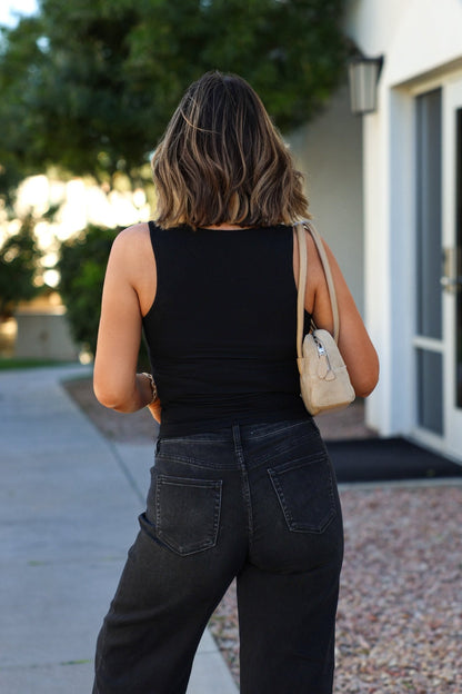Woman with shoulder-length hair walks outdoors in jeans, carrying a beige purse and wearing the Black Square Neck Double Lined Tank Top.