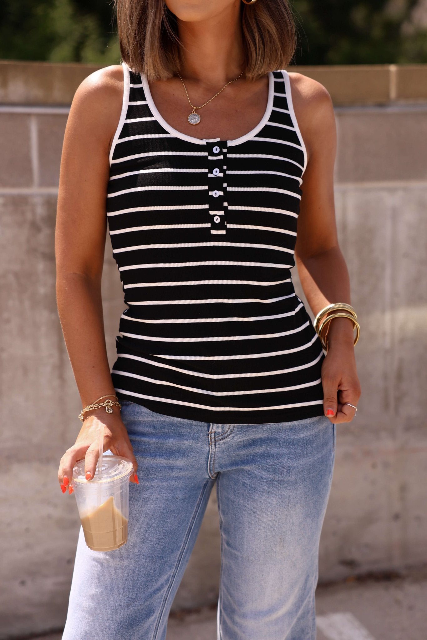 Woman wearing the Black Striped Rib Button Tank Top, jeans, and gold jewelry, holding iced coffee outdoors.