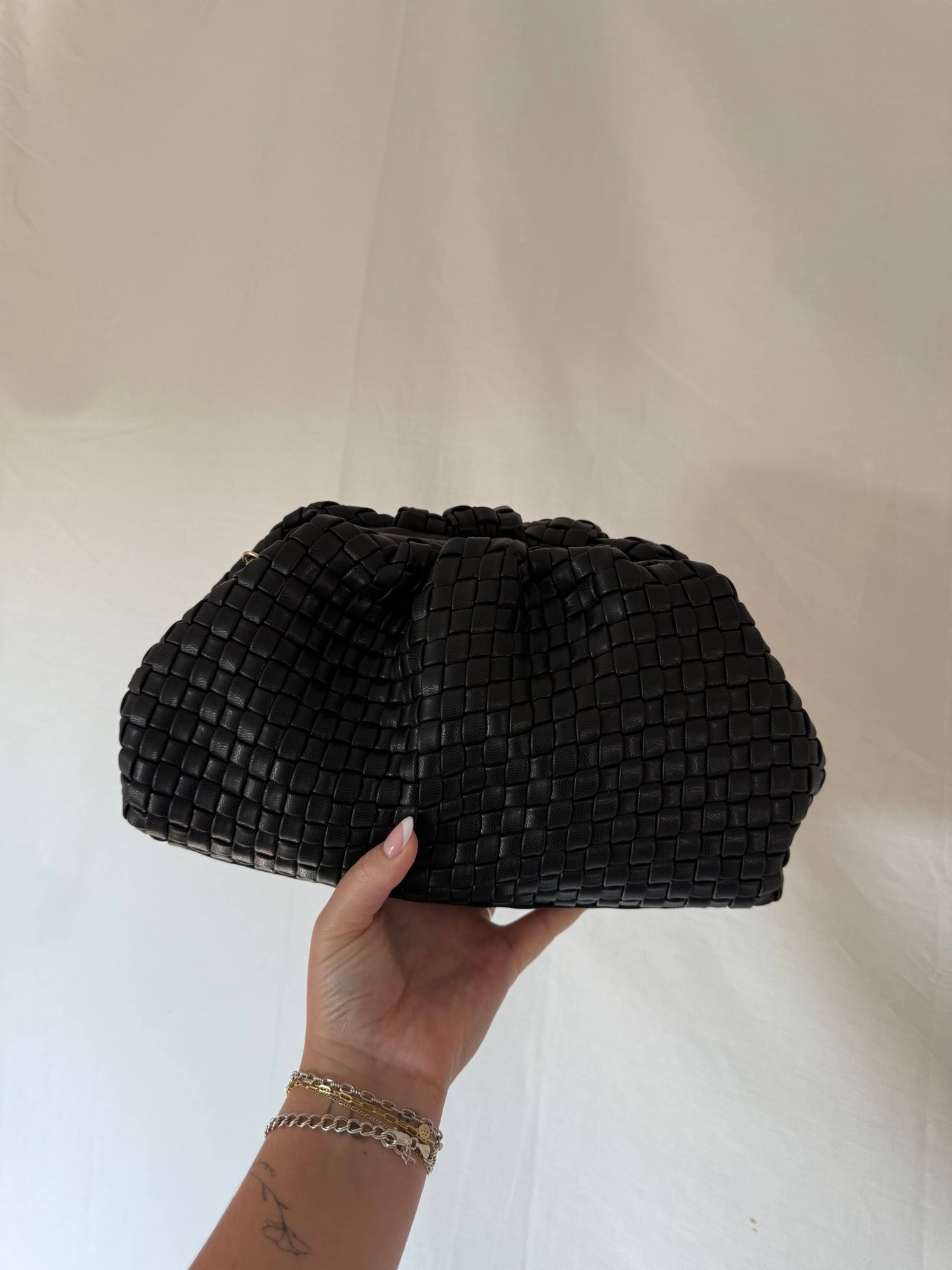 A hand holds the Black Tate Vegan Leather Woven Clutch - FINAL SALE against a plain light background.