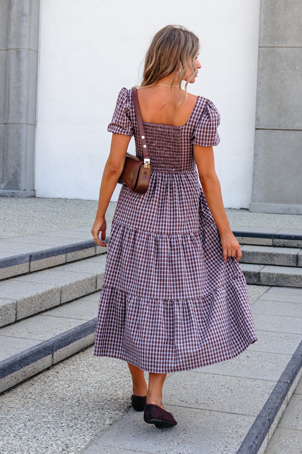 Woman in a BLU PEPPER B6FD1108 MOCHA MIDI DRESS walks up steps with a brown shoulder bag and black flats.