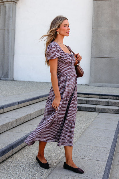 A woman in a BLU PEPPER B6FD1108 MOCHA MIDI DRESS and flats walks outside with a brown bag, her long hair flowing.