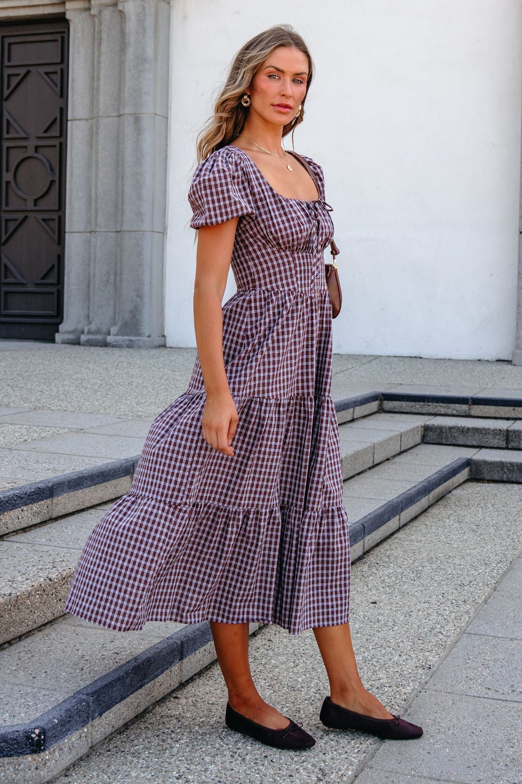 Woman in a BLU PEPPER B6FD1108 MOCHA MIDI DRESS stands on stone steps outdoors, looking at the camera.