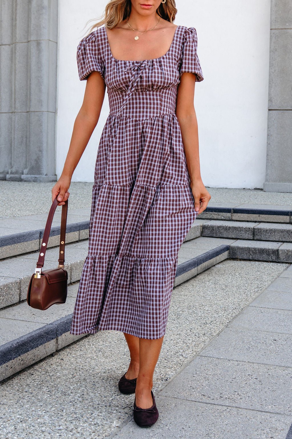 Woman in a mocha BLU PEPPER B6FD1108 midi dress holding a brown handbag, walking outdoors on stone steps.