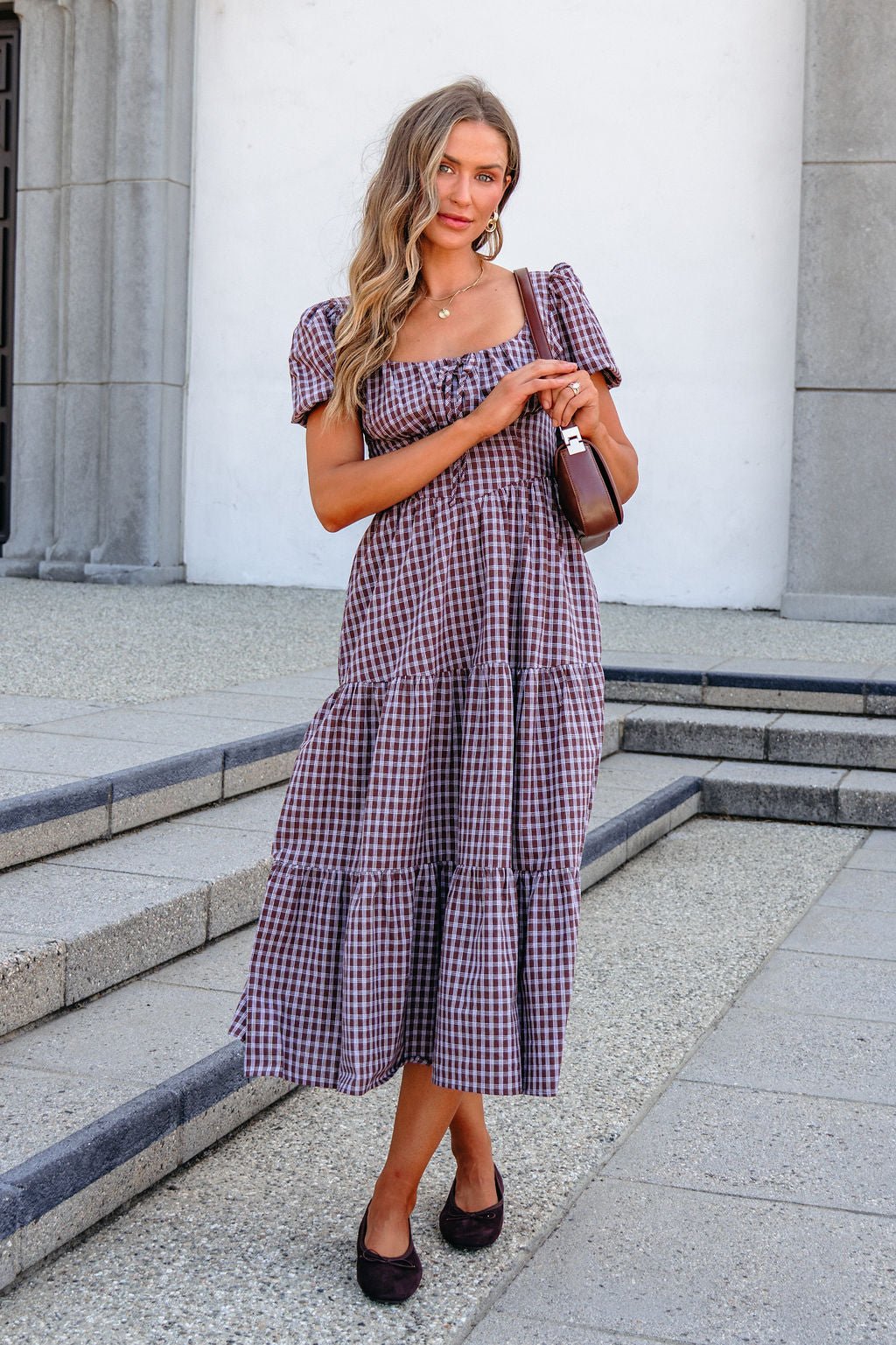 Woman wears a BLU PEPPER B6FD1108 MOCHA MIDI DRESS on stone steps outside, holding a brown handbag and smiling at the camera.