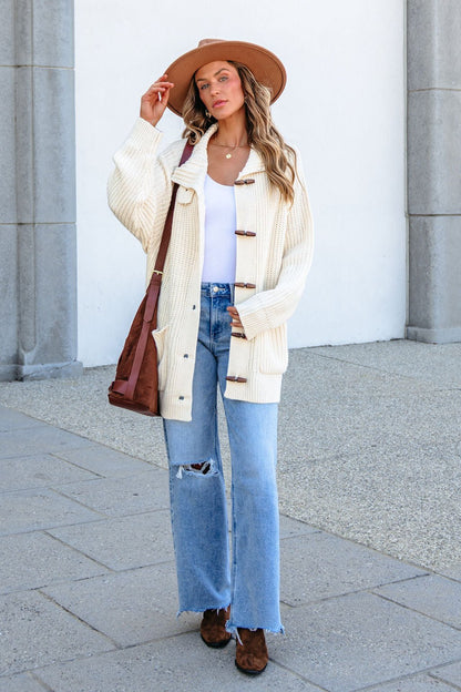 Woman in wide-brimmed hat, BLU PEPPER J6FJ1011 IVORY SWEATER, white top, ripped jeans, boots, and crossbody bag by stone columns.