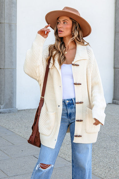 Woman in tan hat, white top, ripped jeans, and BLU PEPPER J6FJ1011 IVORY SWEATER stands by gray stone column.