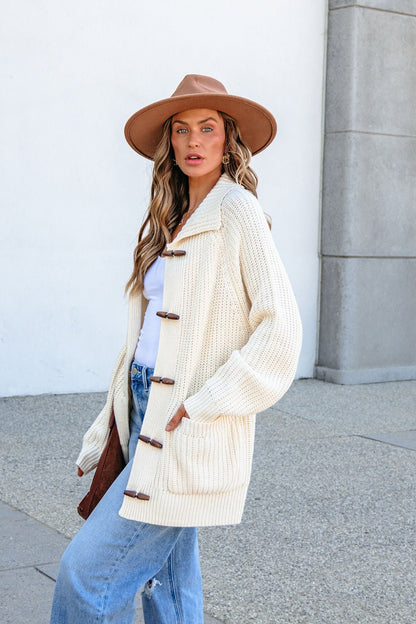 Woman in tan hat, blue jeans, and a BLU PEPPER J6FJ1011 IVORY SWEATER stands outdoors against a light wall, facing the camera.