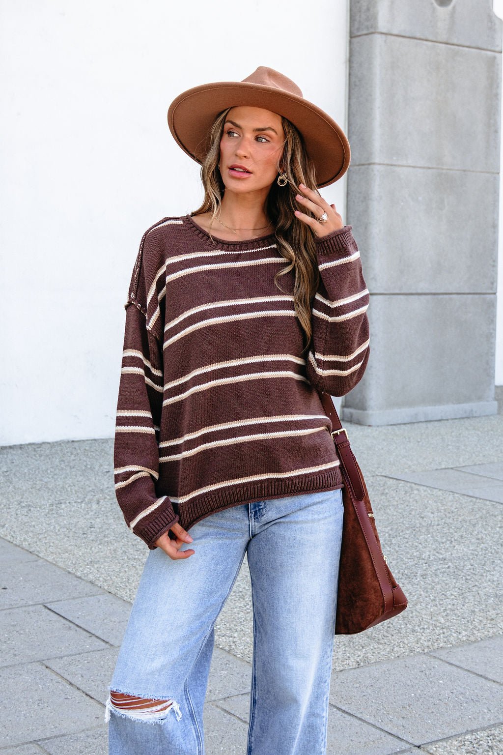 Woman in BLU PEPPER J6FT1014 brown striped sweater and wide-brim hat stands on sidewalk, looking to the side.