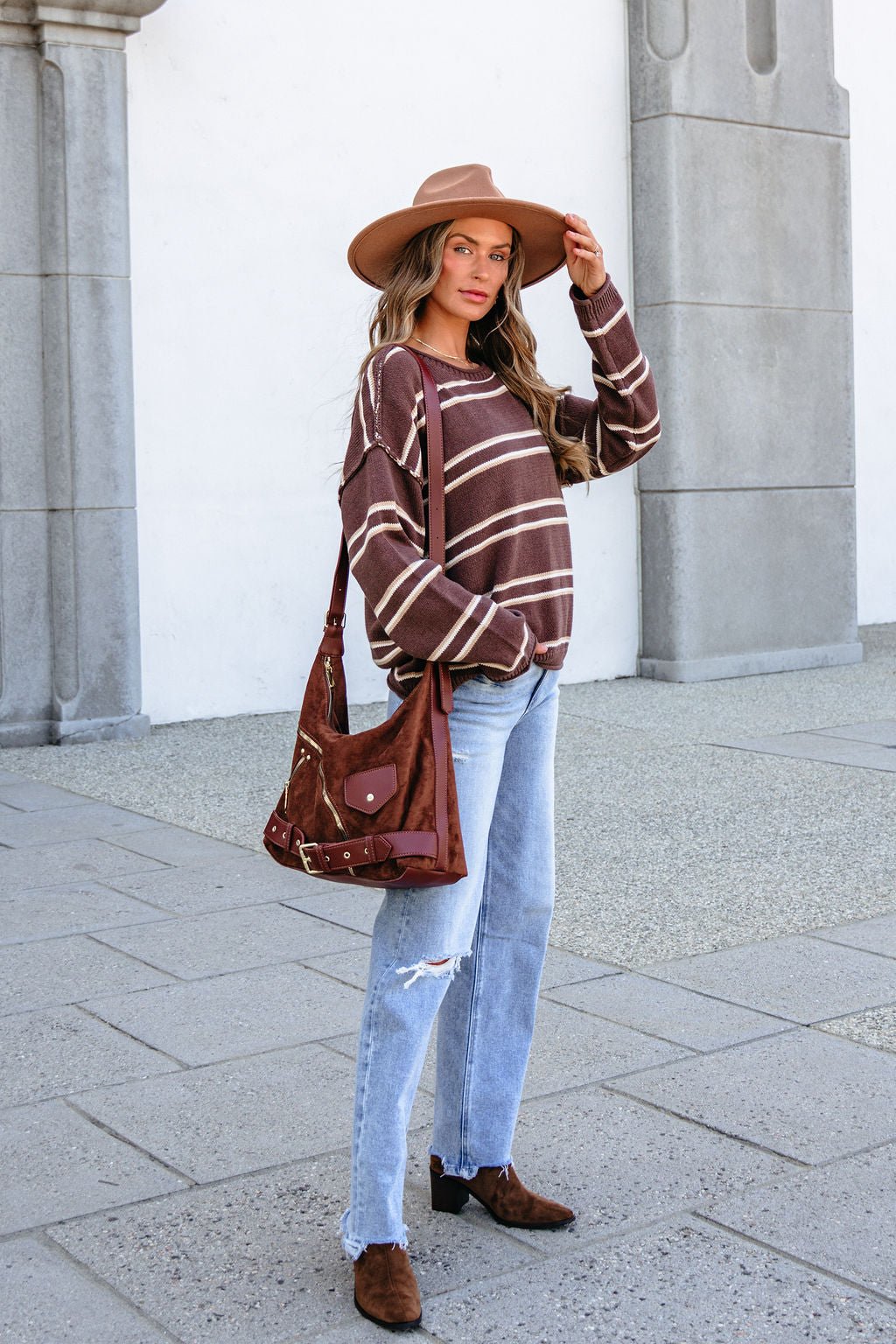 Woman wears a BLU PEPPER J6FT1014 brown striped sweater, ripped jeans, brown hat, boots, and carries a matching brown shoulder bag.