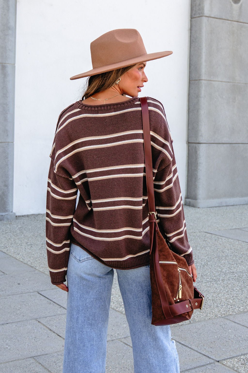 Woman in the BLU PEPPER J6FT1014 BROWN STRIPED SWEATER and blue jeans stands outdoors, facing away.