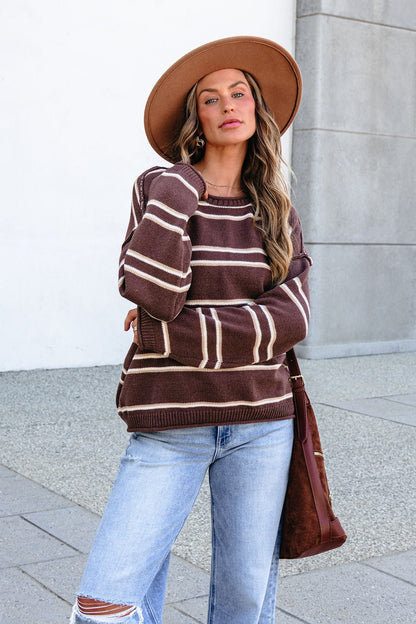 Woman in BLU PEPPER J6FT1014 brown striped sweater, light blue ripped jeans, tan hat, and brown shoulder bag stands outside.