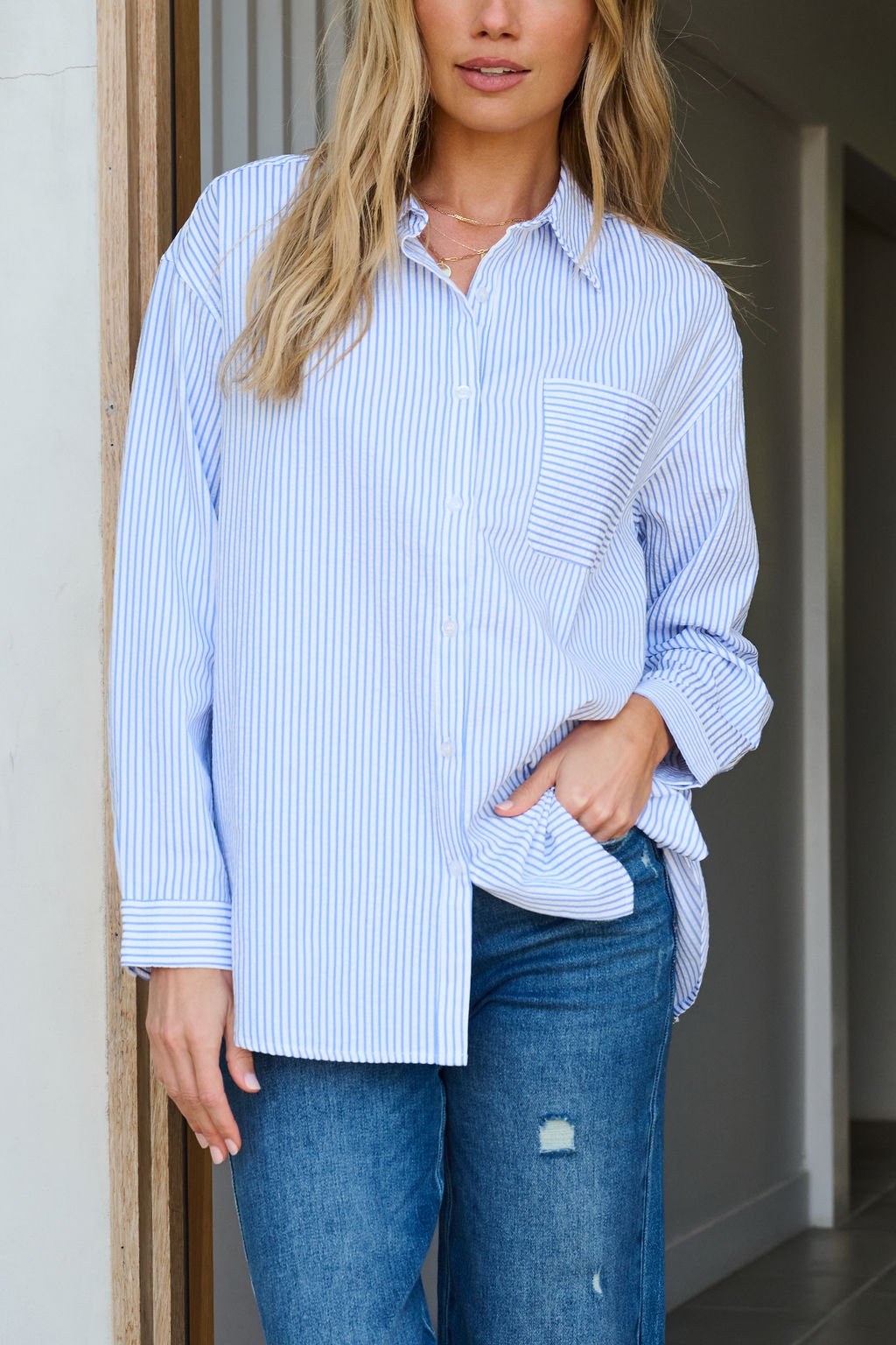 Woman wears a Blue and White Striped Tie Top with blue jeans, standing indoors with one hand in her pocket.