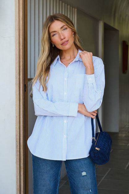 A woman indoors wears a Blue and White Striped Tie Top with jeans, holding a navy handbag.