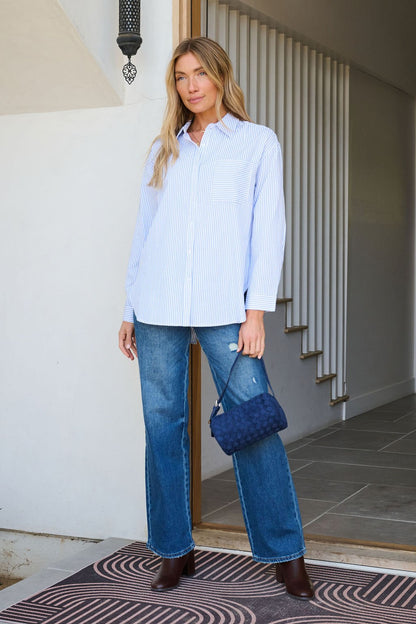 Woman stands indoors wearing the Blue and White Striped Tie Top, blue jeans, brown boots, and a blue quilted handbag.