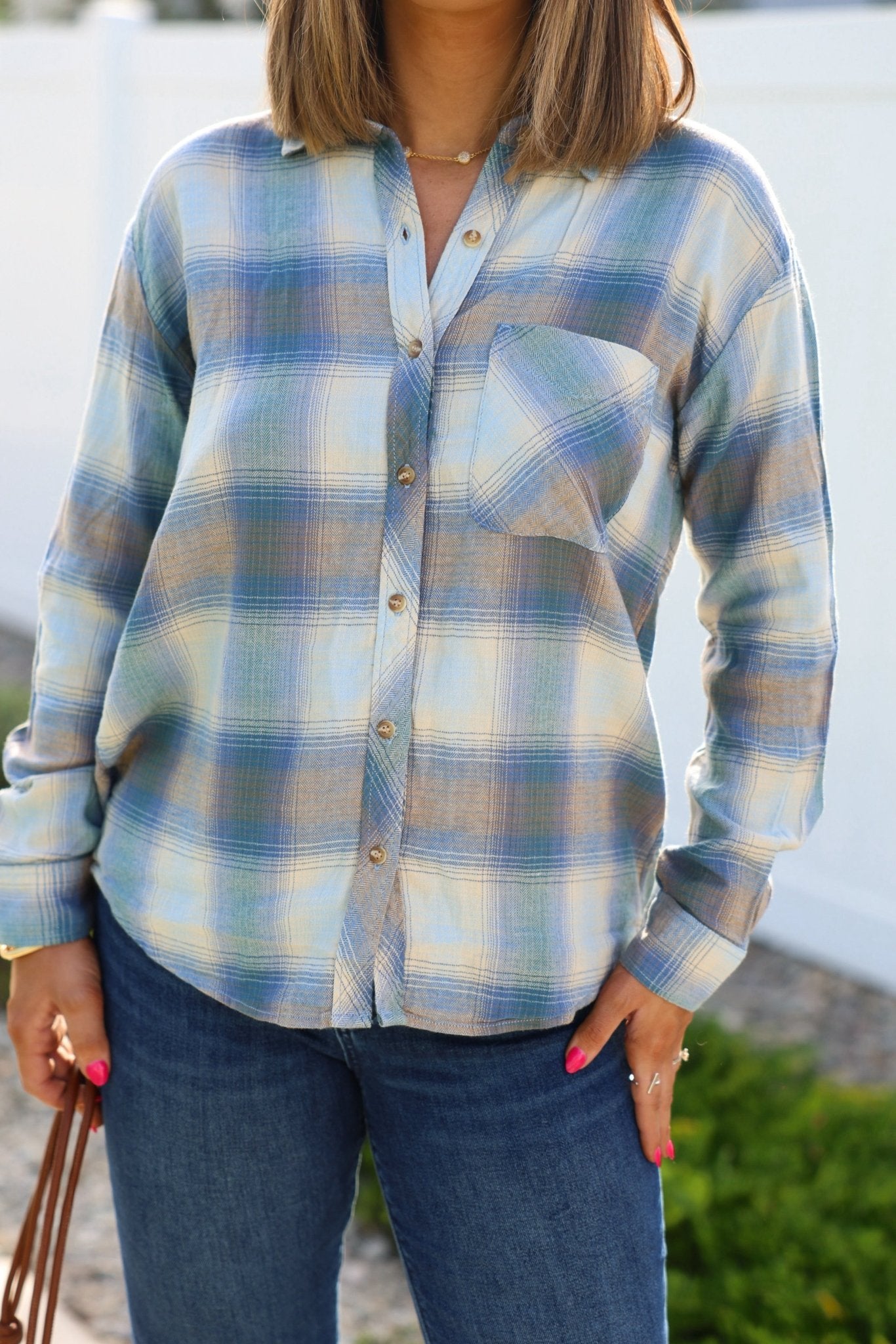 A person wears a Blue Plaid Button Down Flannel Shirt and blue jeans outdoors.