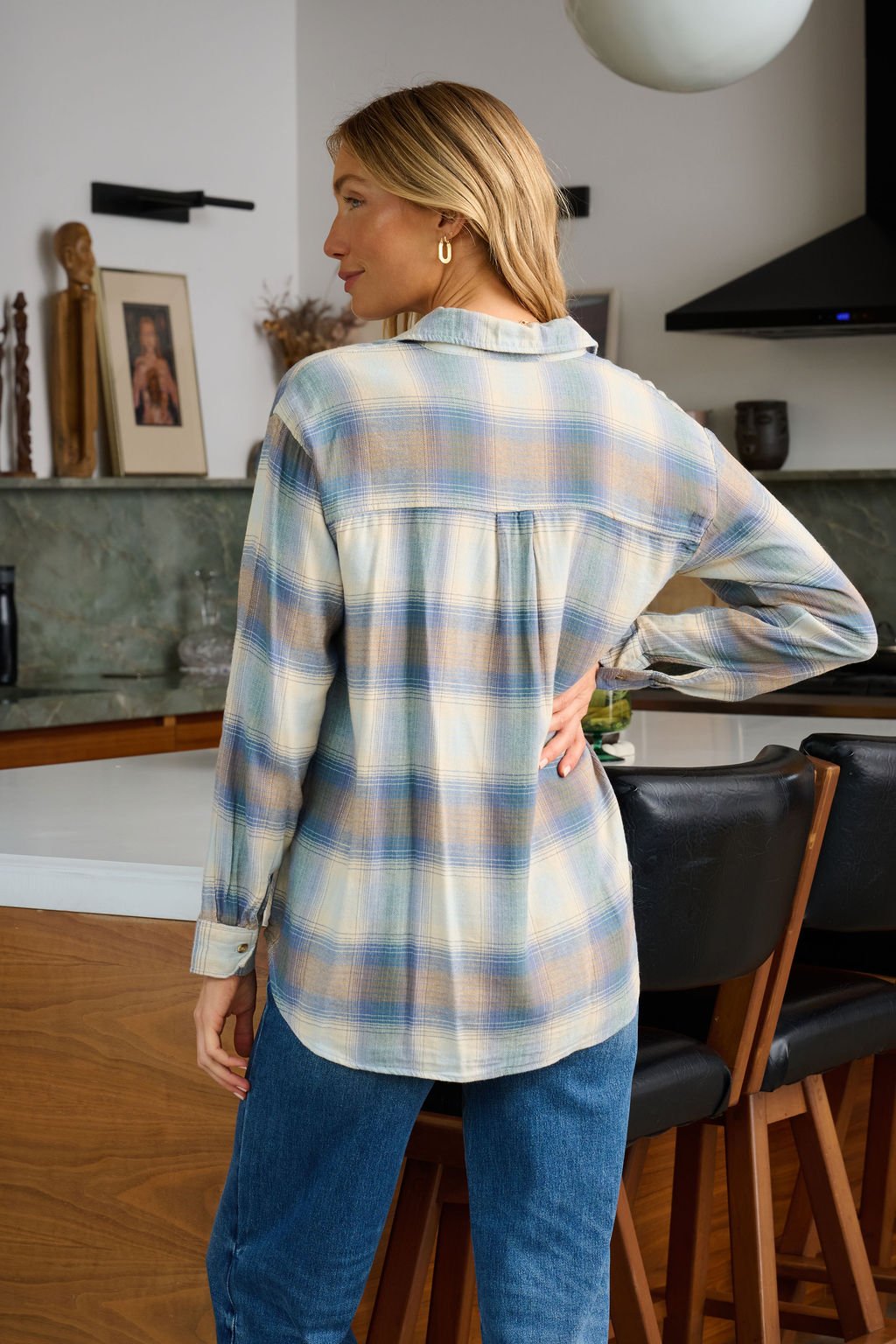 A woman wears a Blue Plaid Button Down Flannel Shirt and jeans in a modern kitchen, her blonde hair visible from behind.