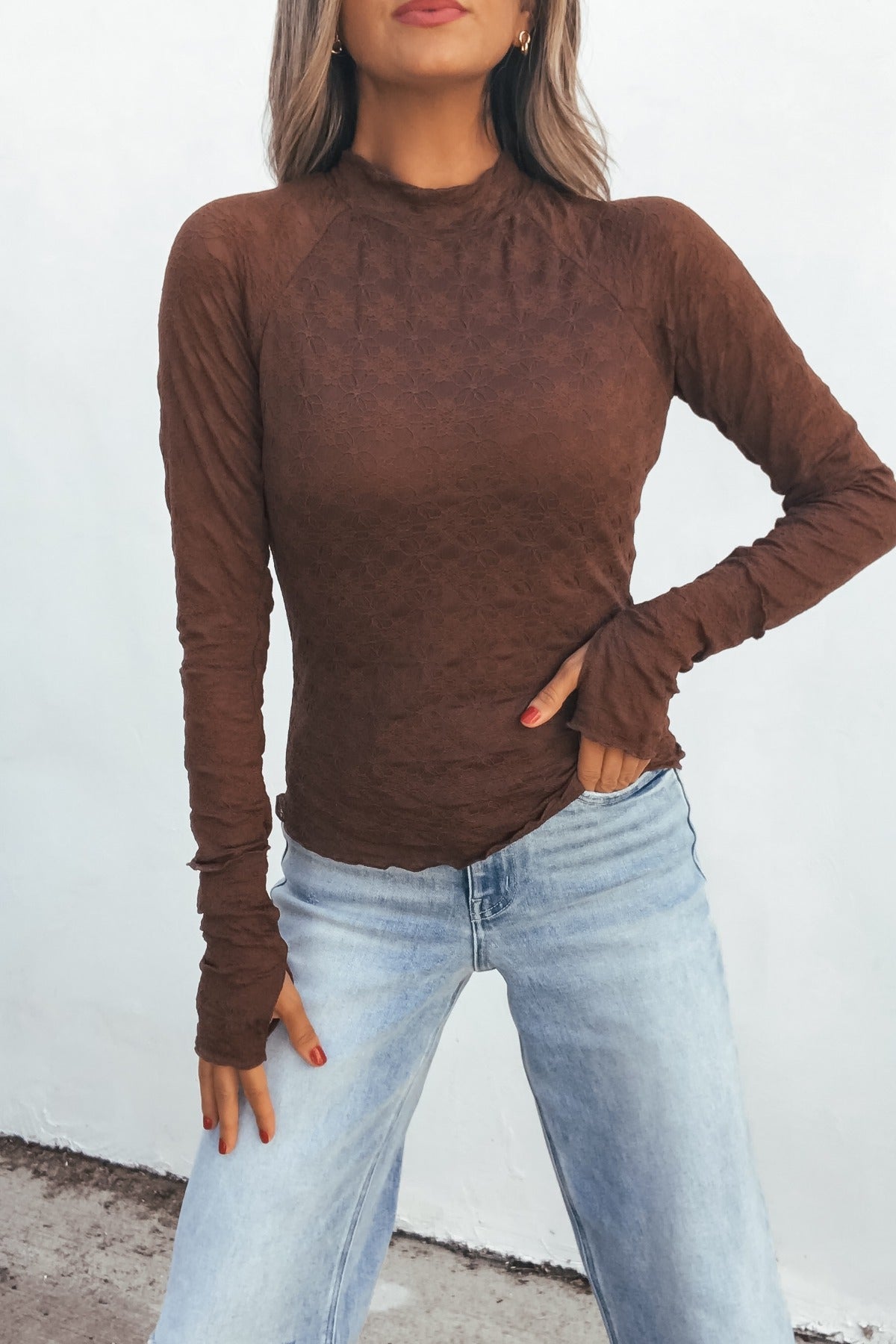 Model in the Bramble Lace Top - Brown and light-wash jeans poses with one hand on her hip against a white background.
