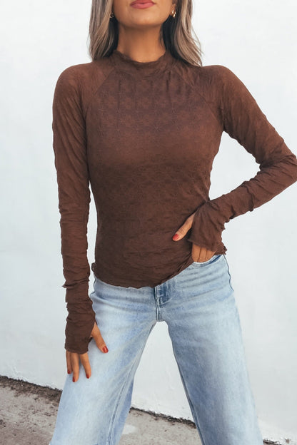 Model in the Bramble Lace Top - Brown and light-wash jeans poses with one hand on her hip against a white background.
