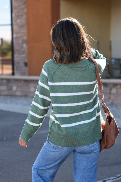 Wearing the Brinkley Sage and White Striped Sweater, someone walks outside with jeans and a brown shoulder bag for fall style.
