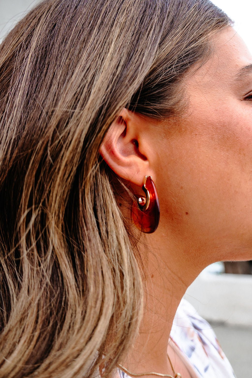 Close-up of a person with light brown hair wearing Brown Abstract Acrylic Hoop Earrings - DOORBUSTER and a thin gold necklace.