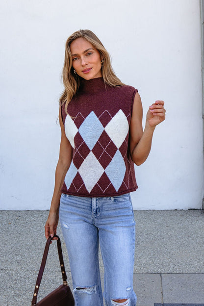 She smiles at the camera outside, wearing a relaxed fit Brown Argyle Sweater Vest with ripped jeans and holding a brown bag.