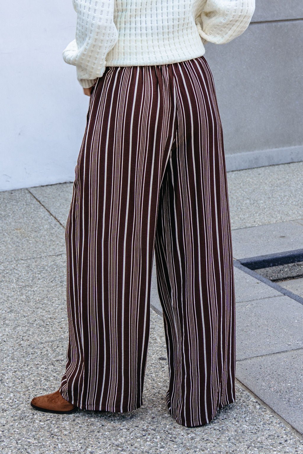 Person wears Brown & Cream Striped Drawstring Pants, a textured white sweater, and brown shoes on concrete.