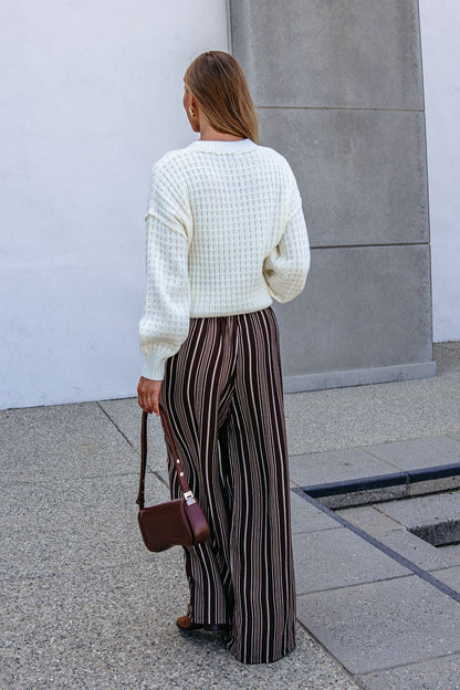 Woman stands outside in a white sweater and Brown & Cream Striped Drawstring Pants, holding a small brown handbag.