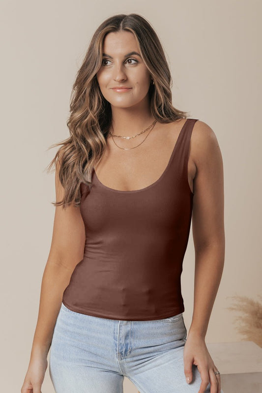 A woman with wavy brown hair models the Brown Double Lined Scoop Neck Jersey Tank with light blue jeans against a neutral background.
