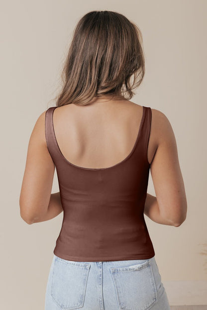 A woman with long brown hair models the Brown Double Lined Scoop Neck Jersey Tank and light blue jeans, back to camera on beige.