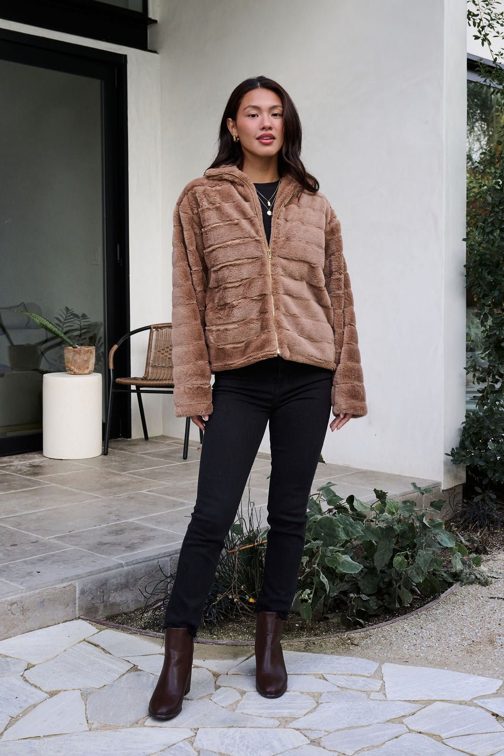 A woman models the Brown Faux Fur Zip Collared Jacket outdoors, highlighting its cozy style.