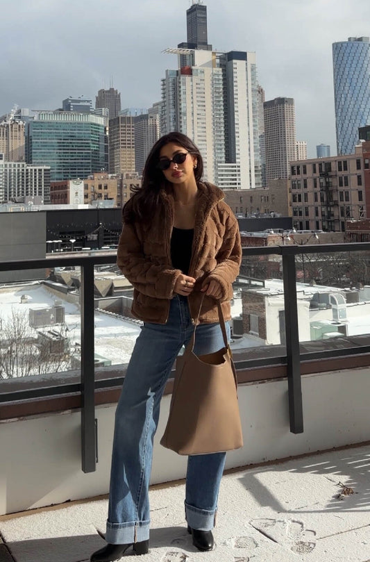 Woman in sunglasses and the Brown Faux Fur Zip Collared Jacket stands on a snowy rooftop with the city skyline behind her.