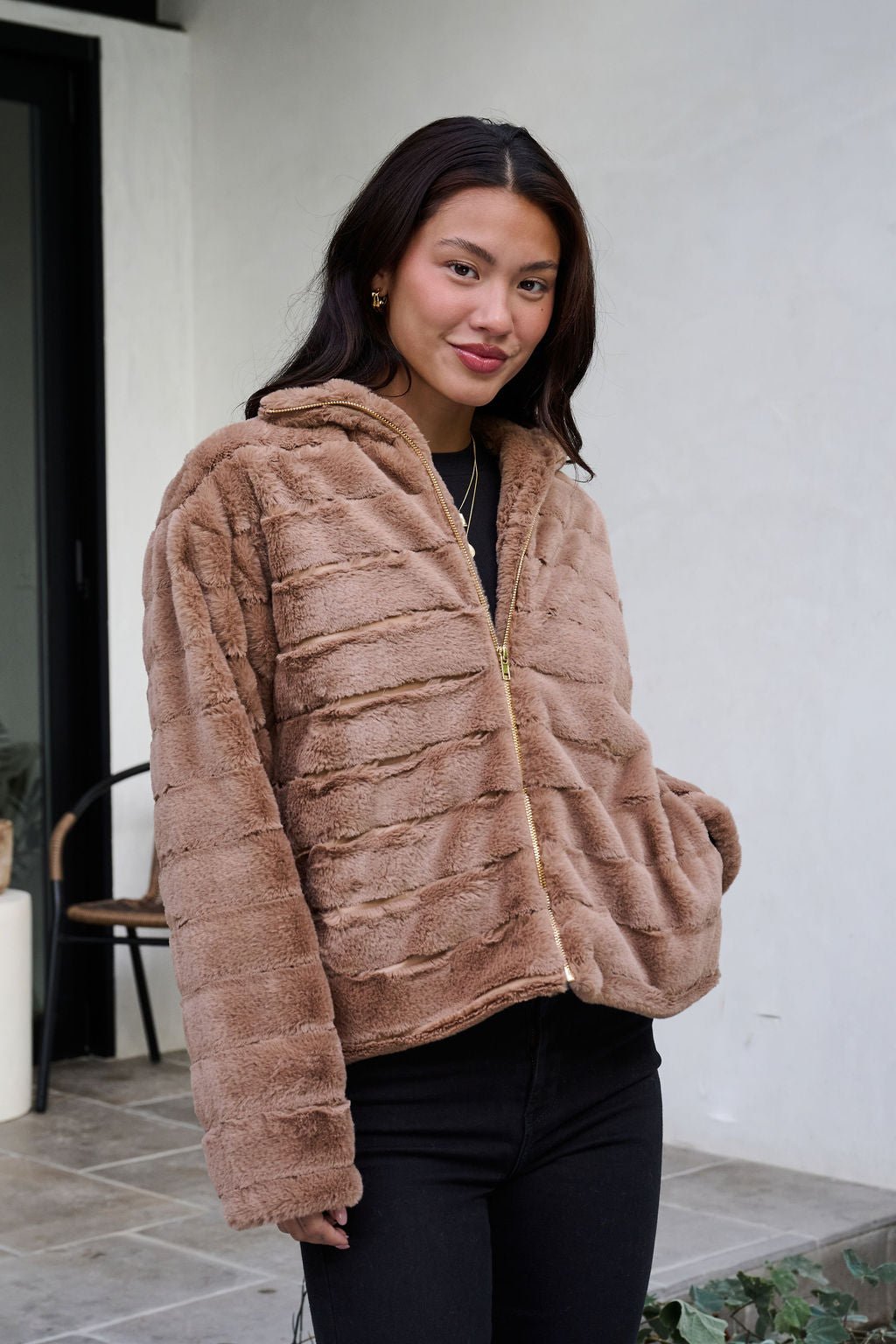 Woman smiles outdoors wearing the Brown Faux Fur Zip Collared Jacket with black pants.