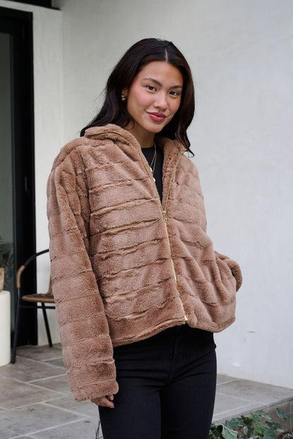 Woman smiles outdoors wearing the Brown Faux Fur Zip Collared Jacket with black pants.