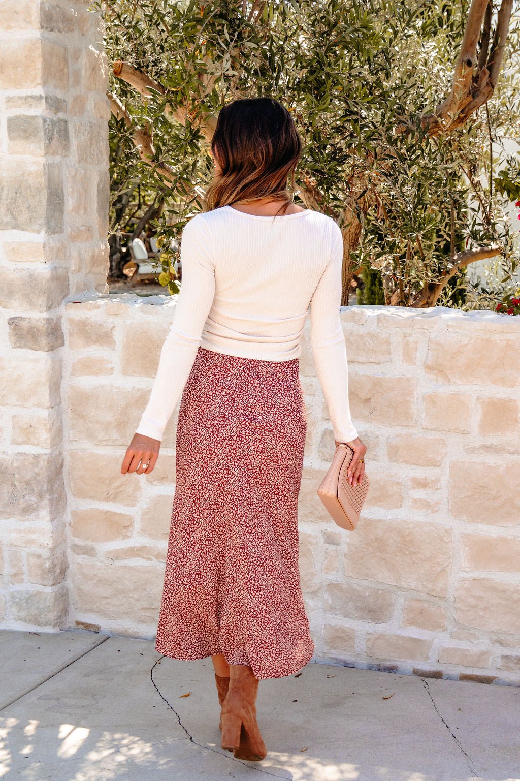 Woman in a white top and Brown Floral Print Midi Skirt stands outdoors with a clutch—perfect choice for your fall wardrobe.