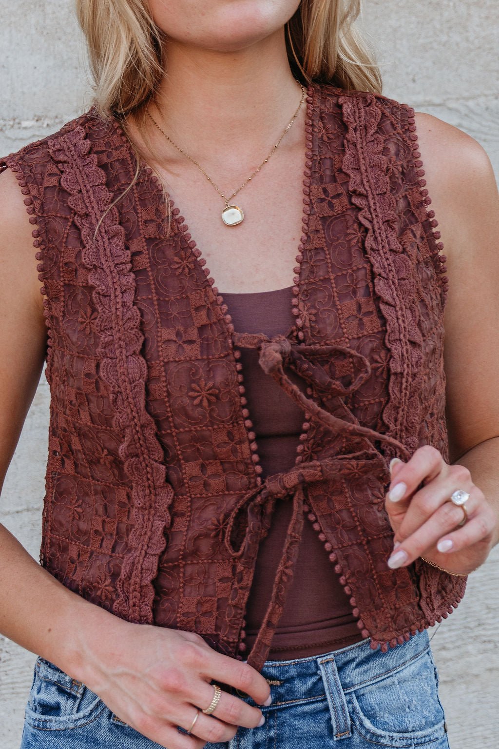 Woman wearing the Brown Lace Eyelet Tie Front Vest - FINAL SALE over a brown top with jeans, accessorized with gold jewelry.