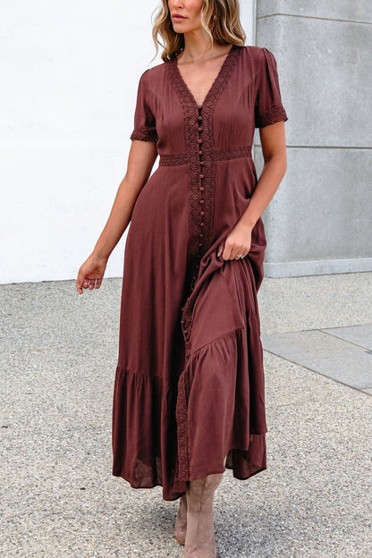Woman wearing a Brown Lace Trim Maxi Dress stands outdoors on a textured surface beside a concrete wall.