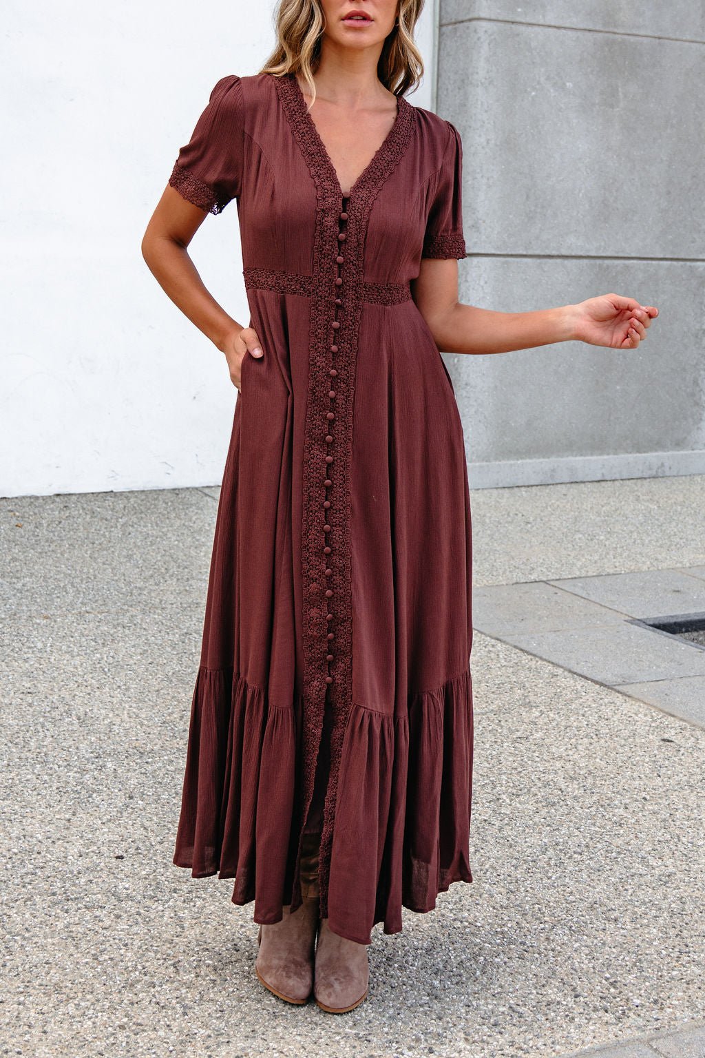Woman in a Brown Lace Trim Maxi Dress and taupe boots stands outdoors on a concrete surface.