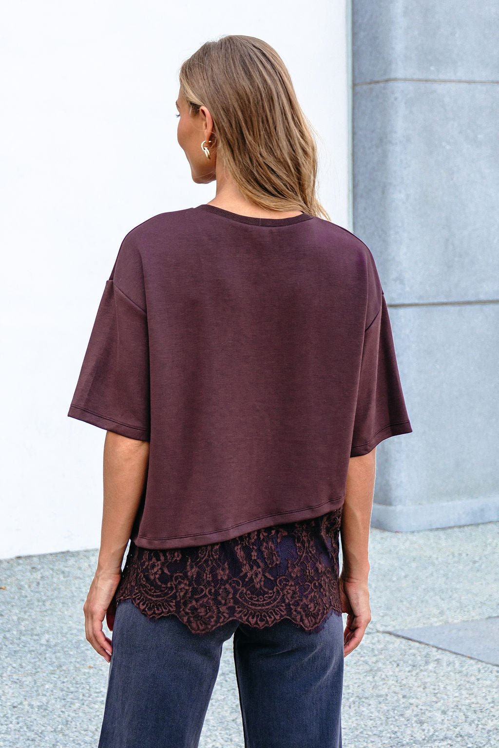 A woman stands outdoors from behind in an oversized maroon top layered over a Brown Lace Trim Short Sleeve Top and dark pants.