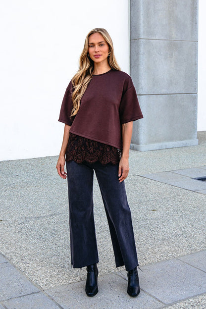 Woman wears a Brown Lace Trim Short Sleeve Top, dark pants, and black boots in an oversized fit while standing outdoors.
