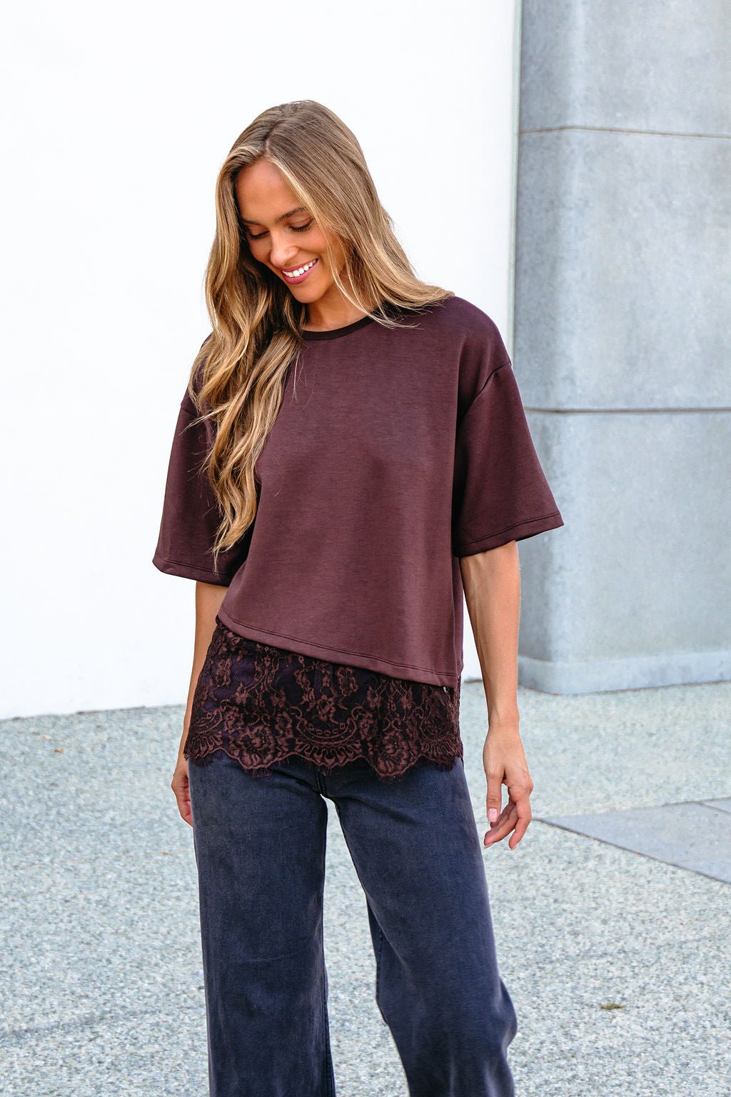 Smiling woman outdoors in a Brown Lace Trim Short Sleeve Top layered over a black shirt, looking down.