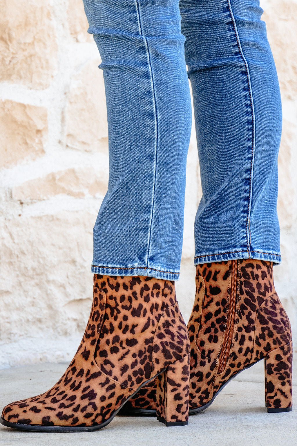 Person wearing blue jeans and Brown Leopard Suede Booties - FINAL SALE, standing on a light-colored surface.
